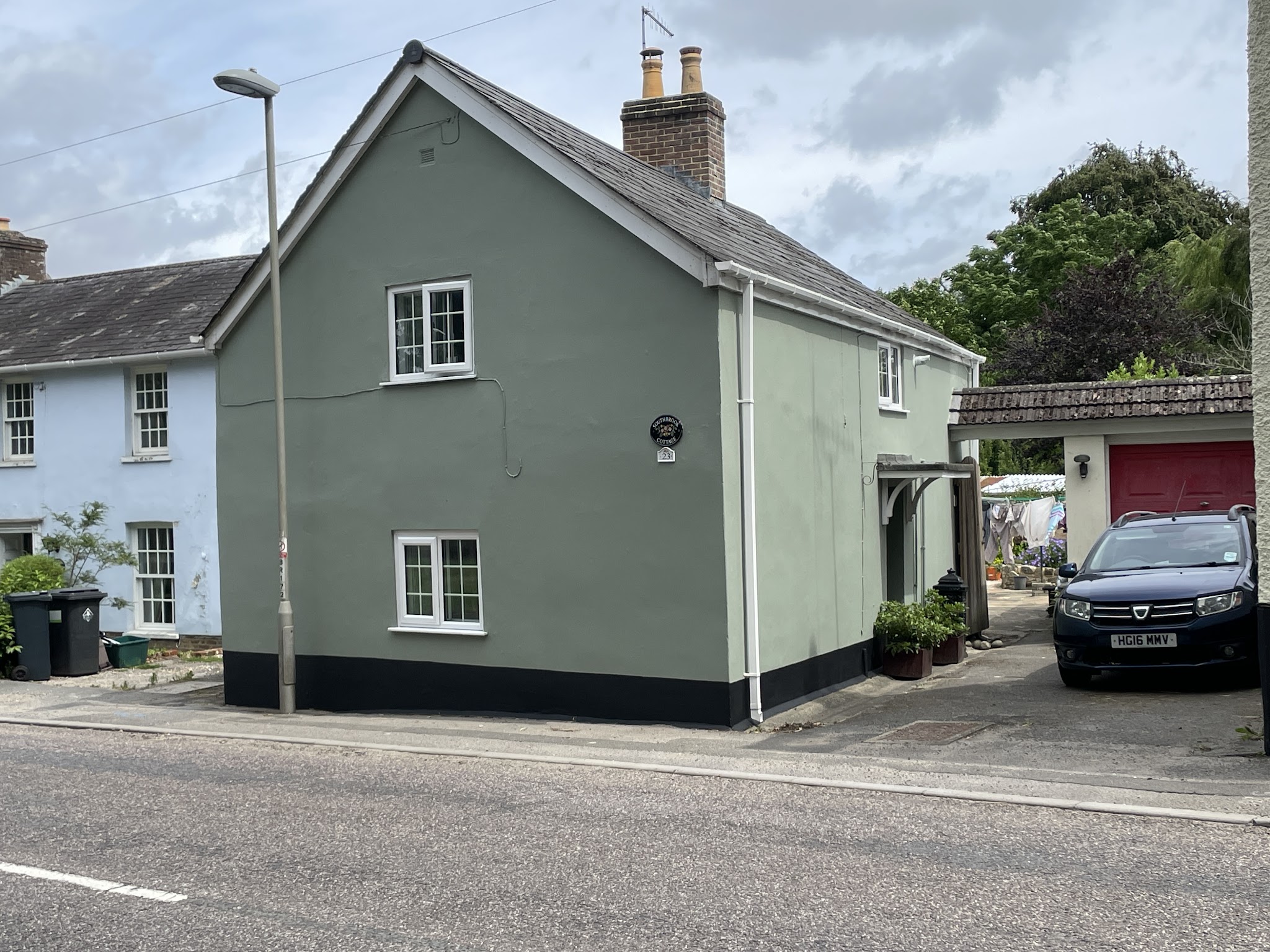 Sage green cottage with a black plinth, freshly painted outside