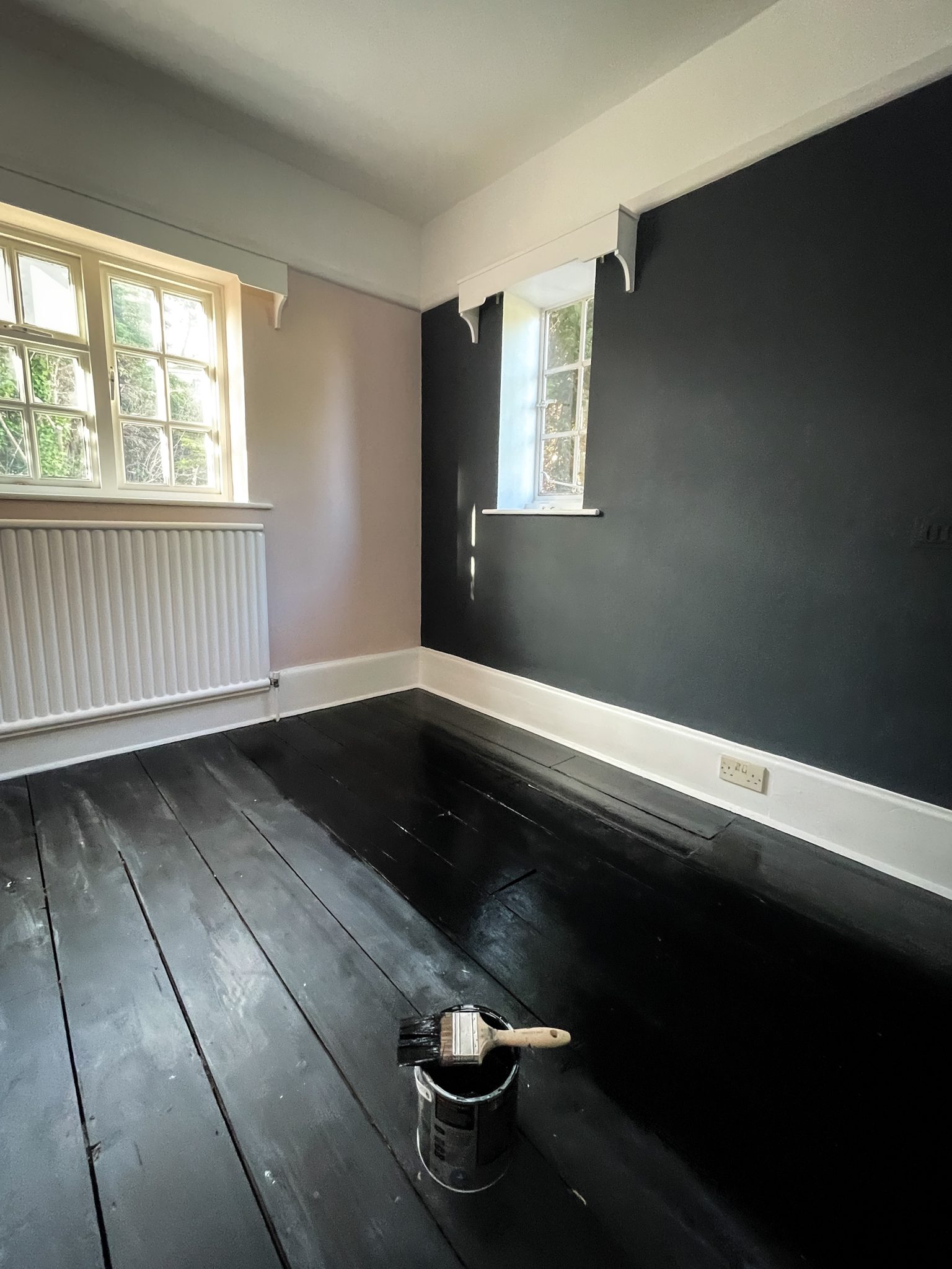Period room with a black feature wall and painted black floorboards, paint tin and brush in shot